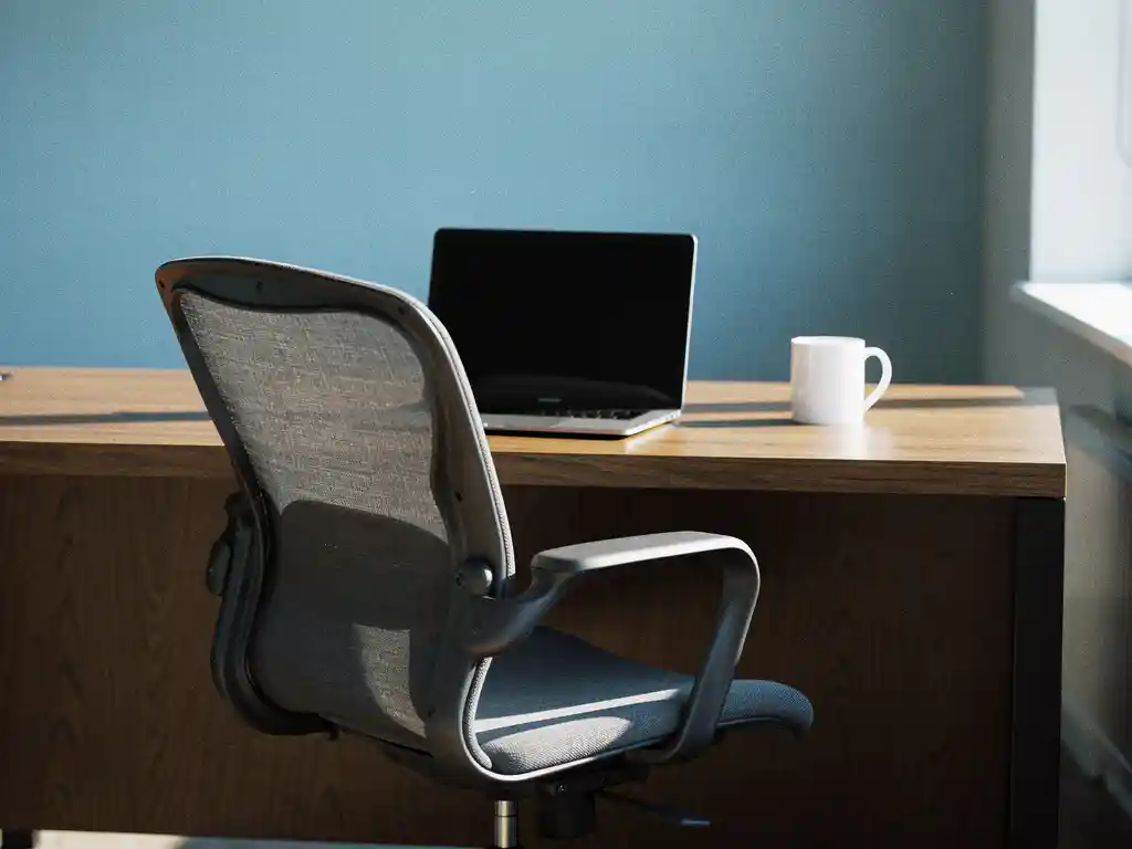 Lege bureaustoel bij houten bureau met laptop en koffiemok, natuurlijk licht door raam